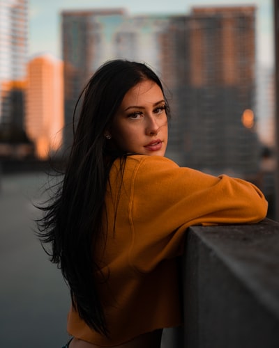 During the day, a woman who is wearing orange hoodie on concrete wall
